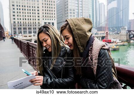 Two friends, outdoors, looking at smartphone, smiling View Large Photo Image Stock Image - Two friends, outdoors, looking at smartphone, smiling. Fotosearch