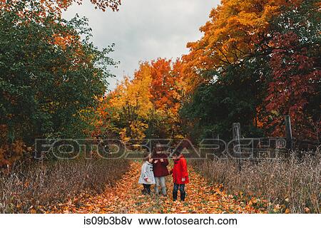 Stock Photo - Two girls and toddler sister looking at autumn leaves on rural path. Fotosearch