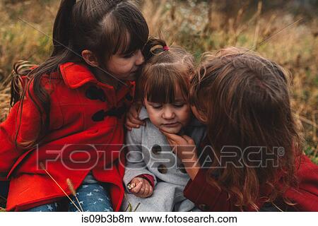 Two girls kissing toddler sister in field View Large Photo Image Picture - Two girls kissing toddler sister in field. Fotosearch