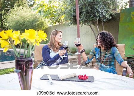 Two mature female friends making a red wine toast at garden table View Large Photo Image Stock Image - Two mature female friends making a red wine toast at garden table. Fotosearch