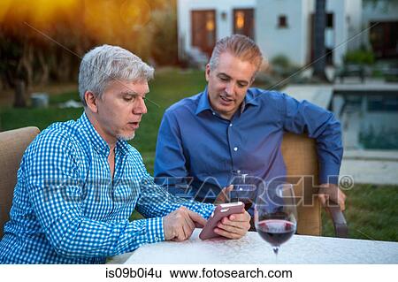Two mature men using smartphone at garden party table View Large Photo Image Stock Photograph - Two mature men using smartphone at garden party table. Fotosearch
