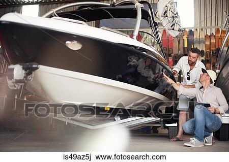 Stock Image - Two men checking motor boat bodywork in repair workshop. Fotosearch