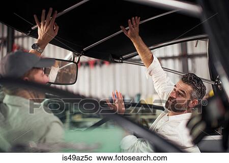 Stock Image - Two men checking roof on boat in repair workshop. Fotosearch