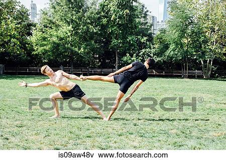 Two men leaning sideways in yoga foot hold position in park View Large Photo Image Stock Photo - Two men leaning sideways in yoga foot hold position in park. Fotosearch