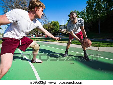 Stock Image - Two men playing basketball on outdoor court. Fotosearch