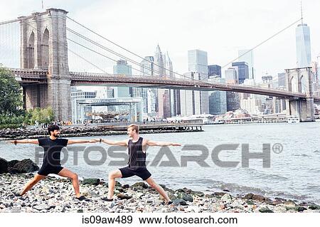 Two men practicing yoga on riverside in front of Brooklyn Bridge, New York, USA View Large Photo Image Stock Photo - Two men practicing yoga on riverside in front of Brooklyn Bridge, New York, USA. Fotosearch