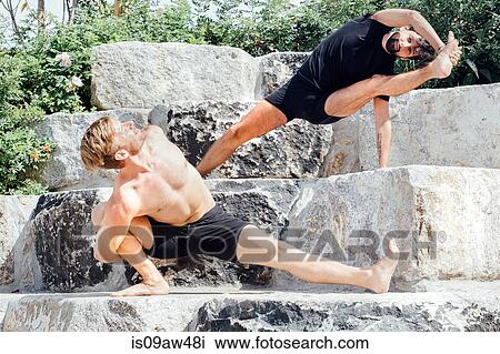 Stock Image - Two men practicing yoga positions on park step. Fotosearch