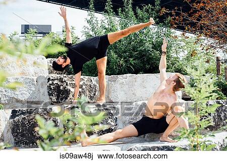 Stock Image - Two men practicing yoga positions together on park step. Fotosearch