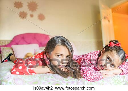 Stock Image - Two sisters lying on bed, pensive expressions. Fotosearch