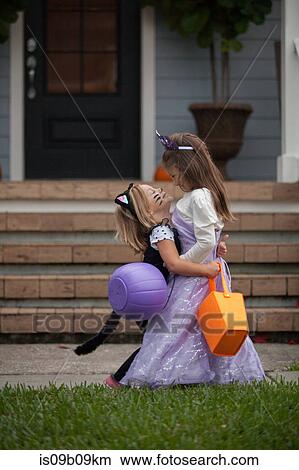 Two sisters trick or treating in cat and fairy costumes hugging at porch stairway View Large Photo Image Picture - Two sisters trick or treating in cat and fairy costumes hugging at porch stairway. Fotosearch