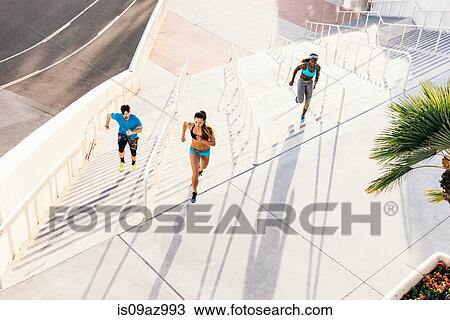 Stock Image - Two women and man training, running up sport facility stairway, downtown San Diego, California, USA. Fotosearch