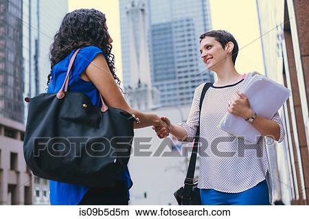 Two women, outdoors, shaking hands, low angle view View Large Photo Image Picture - Two women, outdoors, shaking hands, low angle view. Fotosearch