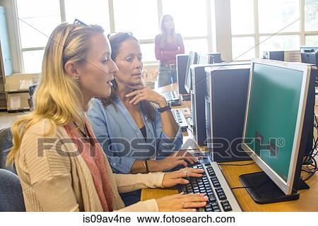 Stock Image - Two women searching computer data for books in library. Fotosearch