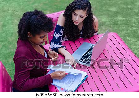 Two women sitting outdoors, looking at paperwork, using laptop View Large Photo Image Stock Image - Two women sitting outdoors, looking at paperwork, using laptop. Fotosearch