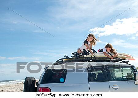 Two young girls securing surfboards to top of car View Large Photo Image Stock Photography - Two young girls securing surfboards to top of car. Fotosearch