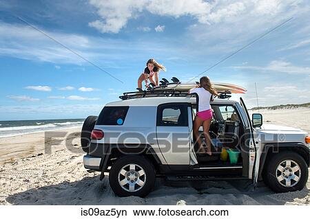 Two young girls untying surfboards from top of car View Large Photo Image Picture - Two young girls untying surfboards from top of car. Fotosearch