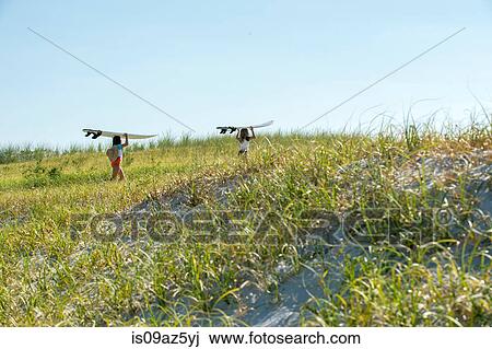 Two young girls walking on sand dunes, carrying surfboards View Large Photo Image Stock Image - Two young girls walking on sand dunes, carrying surfboards. Fotosearch
