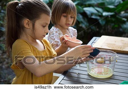 Stock Image - Two young sisters pouring lemon juice for lemonade at garden table. Fotosearch