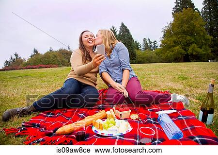 Two young women enjoying picnic in park, fooling around, taking selfie, using smartphone View Large Photo Image Stock Image - Two young women enjoying picnic in park, fooling around, taking selfie, using smartphone. Fotosearch