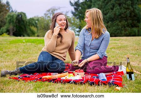 Two young women enjoying picnic in park, using smartphone View Large Photo Image Stock Image - Two young women enjoying picnic in park, using smartphone. Fotosearch