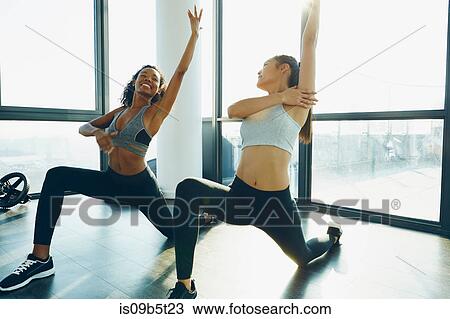 Stock Image - Two young women exercising in gym, doing lunges. Fotosearch