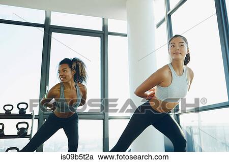 Stock Image - Two young women exercising in gym, doing aerobic workout. Fotosearch
