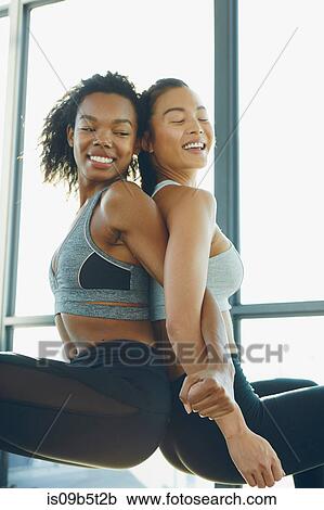 Stock Image - Two young women exercising in gym, doing squats, back to back. Fotosearch