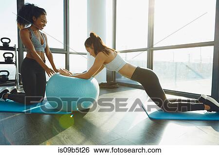 Stock Photograph - Two young women exercising in gym, using inflatable exercise ball. Fotosearch