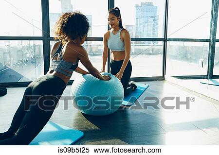 Stock Photography - Two young women exercising in gym, using inflatable exercise ball. Fotosearch