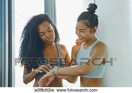Two young women in gym, looking at activity tracker View Large Photo Image Stock Photo - Two young women in gym, looking at activity tracker. Fotosearch