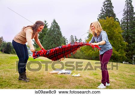 Two young women setting out picnic blanket in park View Large Photo Image Stock Photo - Two young women setting out picnic blanket in park. Fotosearch