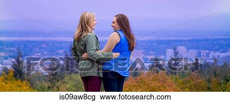 Two young women, standing on hillside, arms around each other, smiling View Large Photo Image Stock Image - Two young women, standing on hillside, arms around each other, smiling. Fotosearch