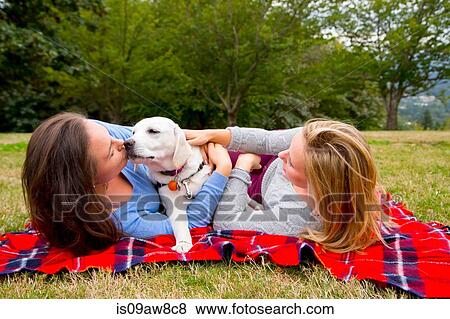 Two young women with pet dog, lying on blanket in park View Large Photo Image Stock Photo - Two young women with pet dog, lying on blanket in park. Fotosearch