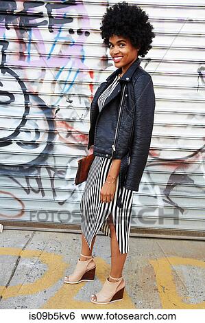 Stock Photograph - Urban portrait of young female fashion blogger with afro hair by graffiti wall, New York, USA. Fotosearch