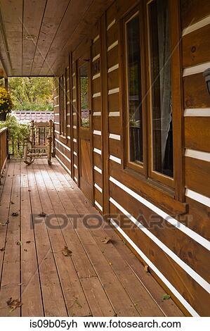 Stock Image - Veranda with rocking chair on facade of rustic Canadian cottage style log home in autumn, Quebec, Canada. Fotosearch