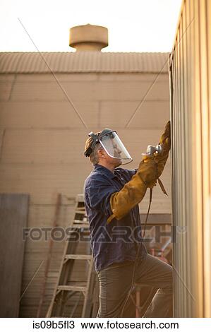 Stock Image - Welder using power tool on shipping container. Fotosearch