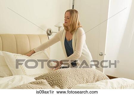 Stock Photography - Woman arranging pillows whilst making bed. Fotosearch