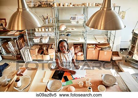 Stock Photography - Woman at desk in pottery studio with paperwork. Fotosearch