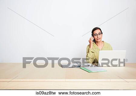 Woman at desk using phone and laptop View Large Photo Image Stock Photo - Woman at desk using phone and laptop. Fotosearch