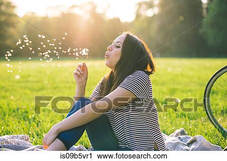 Stock Image - Woman blowing dandelion on grass. Fotosearch