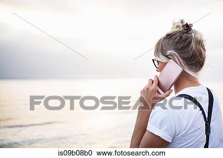 Stock Image - Woman by ocean making telephone call on smartphone, Encinitas, California, USA. Fotosearch