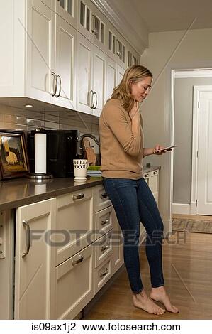 Stock Image - Woman concentrating whilst reading smartphone text in kitchen. Fotosearch