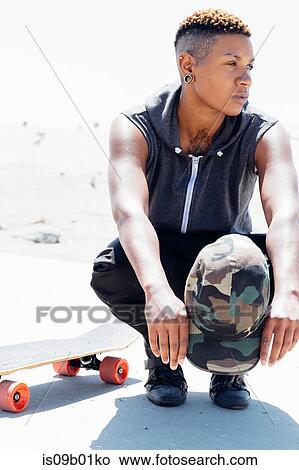 Picture - Woman crouching by skateboard looking away. Fotosearch