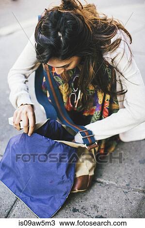 Woman crouching on pavement looking down searching though hip bag View Large Photo Image Stock Image - Woman crouching on pavement looking down searching though hip bag. Fotosearch