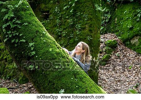 Stock Photography - Woman gazing up at moss covered tree, Spain. Fotosearch