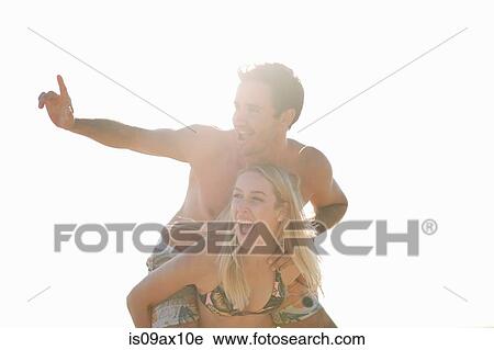 Stock Image - Woman giving man piggyback looking away smiling. Fotosearch