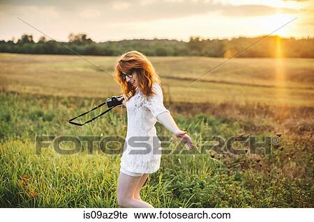 Stock Image - Woman holding camera in field. Fotosearch