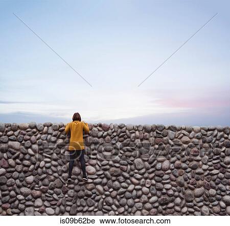 Stock Image - Woman holding onto stone wall, looking over top. Fotosearch