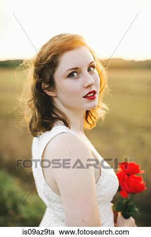 Woman holding red flowers looking over shoulder at camera View Large Photo Image Stock Image - Woman holding red flowers looking over shoulder at camera. Fotosearch