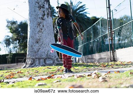 Woman holding skateboard in park View Large Photo Image Stock Photo - Woman holding skateboard in park. Fotosearch